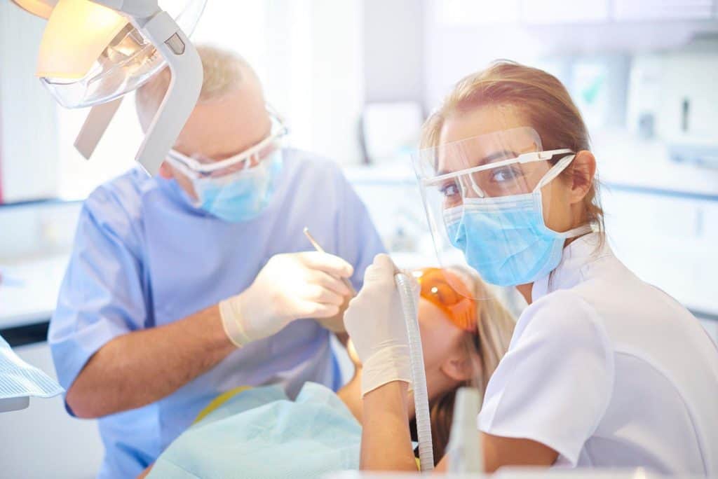 A dentist and dental assistant in protective gear performing a dental procedure on a patient at Los Algodones Dentists Guide