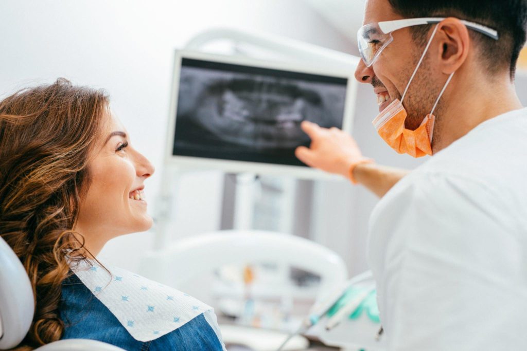 Smiling female patient in dental chair with dentist checking dental x-ray